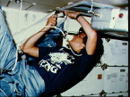 Dr. Sally K. Ride on the middeck of the Space Shuttle Challenger. Her shirt features a cartoon of 35 busy astronauts around a shuttle with the acronym TFNG, which stands for thirty five new guys, a nickname for the 1978 astronaut class. 